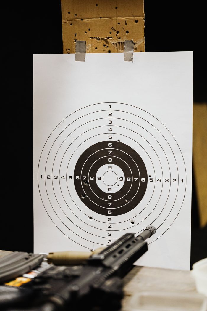 Paper target with bullet holes at a shooting range, firearm visible.